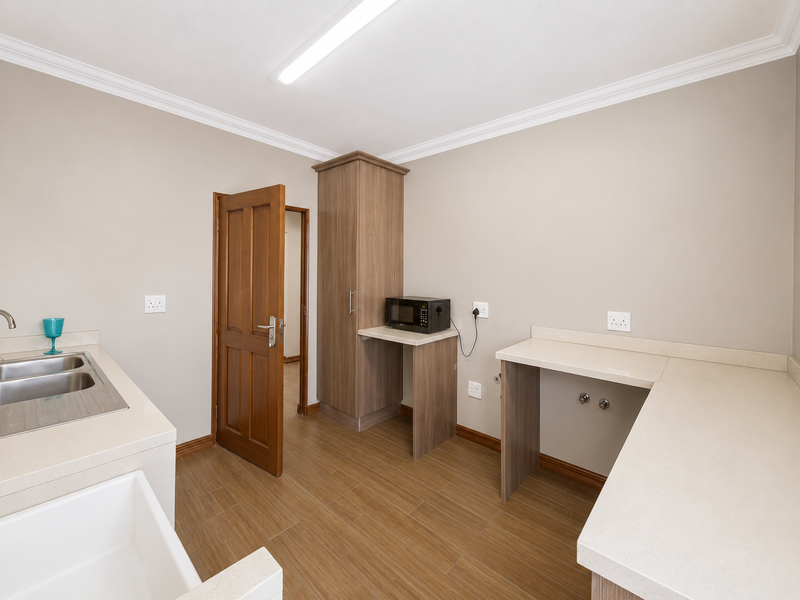 A clean and functional laundry room featuring built-in cabinetry, stone countertops, a double sink, and tiled flooring with dedicated plumbing connections.