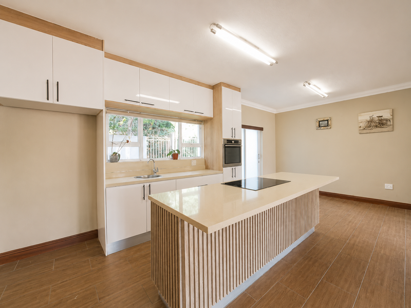 Modern kitchen featuring a central island with stone countertop, built-in oven, electric cooktop, ample cabinetry, and tiled flooring in an open-plan layout.