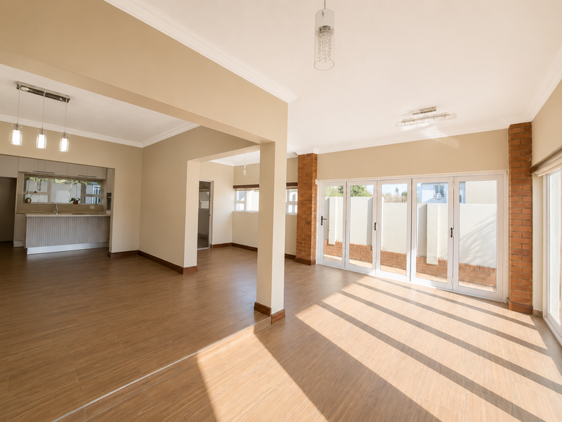 Spacious open-plan living and kitchen area featuring wood-look tiled floors, exposed brick accents, and large folding glass doors leading to the exterior.