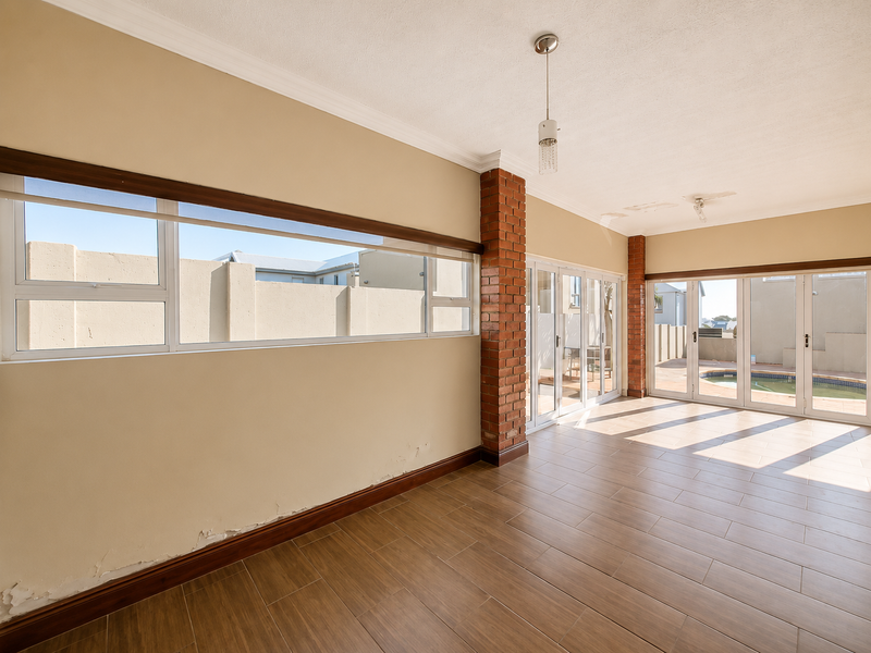 Spacious living area featuring exposed brick pillars, tiled flooring, and large aluminium sliding doors providing access to the pool area.