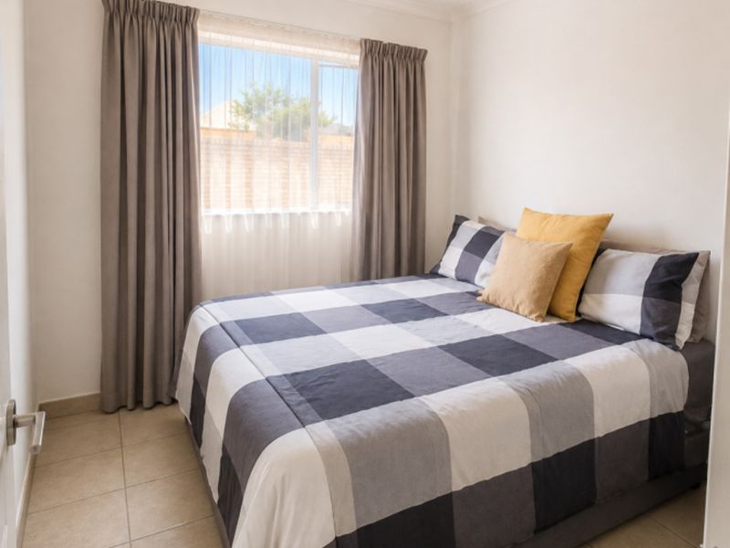 A compact bedroom featuring neutral tiled flooring, a central ceiling light fixture, and a window with curtains.