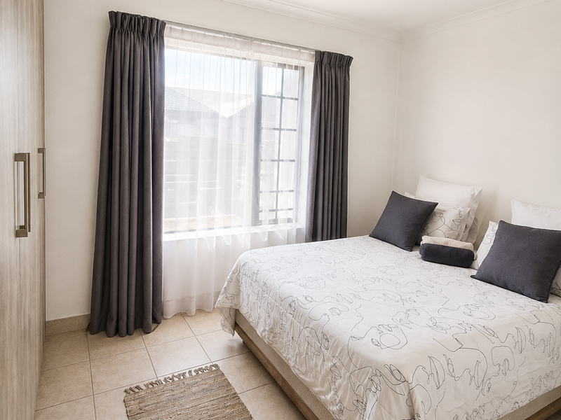 A well-maintained bedroom featuring neutral tiled flooring, a built-in wardrobe, and a ceiling-mounted spotlight fixture, offering a clean and functional living space.