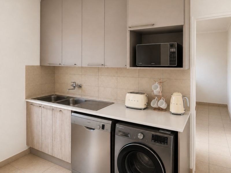 A compact, modern kitchen featuring neutral-toned cabinetry, tiled backsplash, double sink, and integrated space for laundry and dishwashing appliances.