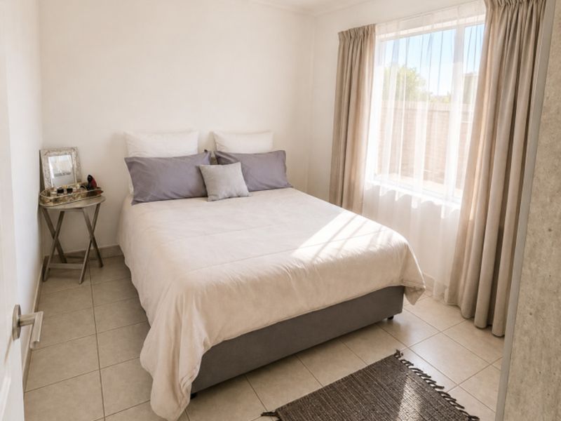A bright and tidy bedroom featuring neutral tiled flooring, a modern ceiling spotlight fixture, and large windows with installed curtain tracks.
