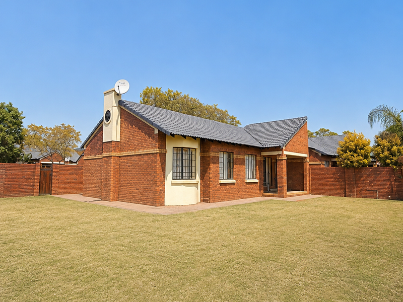 A well-maintained townhouse featuring a face brick exterior, tiled roof, and a spacious private lawn area enclosed by brick boundary walls.