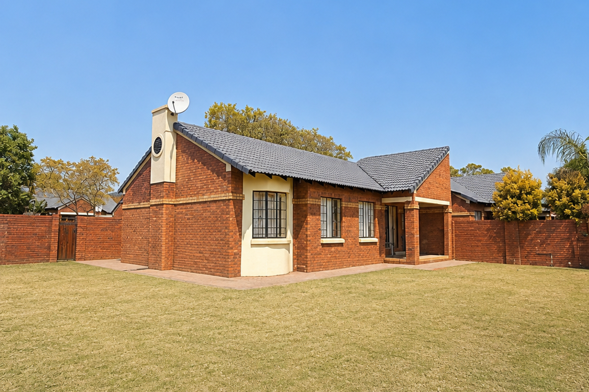 A well-maintained townhouse featuring a face brick exterior, tiled roof, and a spacious private lawn area enclosed by brick boundary walls.