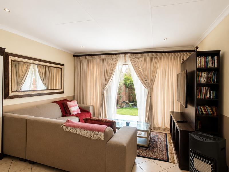 A well-maintained living room featuring tiled flooring, recessed downlighting, and direct access to the rear garden through sliding glass doors.