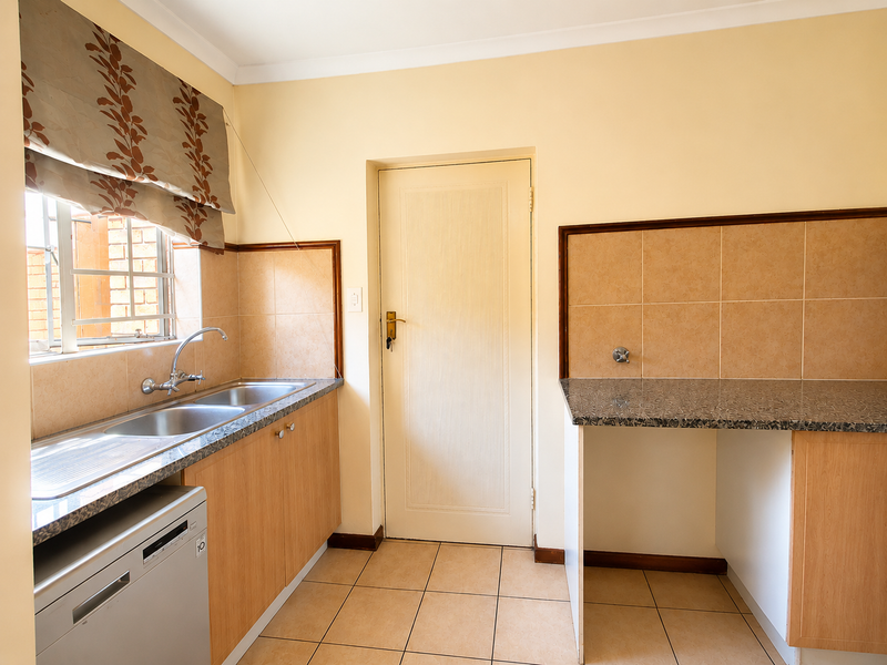 Functional scullery area featuring double stainless steel sink, laminate cabinetry, granite-look countertops, and tiled finishes, providing practical utility space.