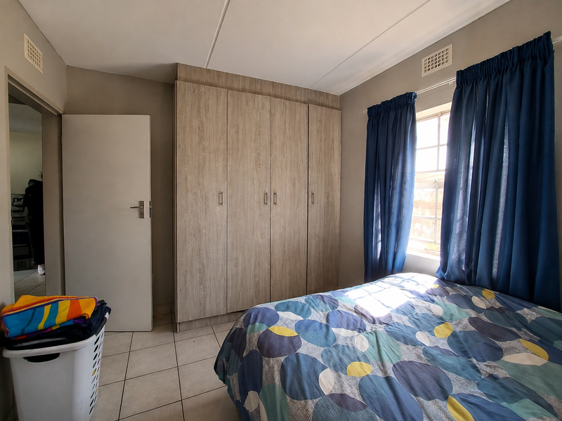 A bedroom featuring built-in wooden cupboards, tiled flooring, and natural light from a window with curtains.