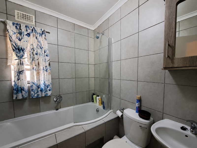 A functional bathroom featuring a bathtub with a glass shower screen, a pedestal basin, and a toilet, finished with neutral wall and floor tiles.