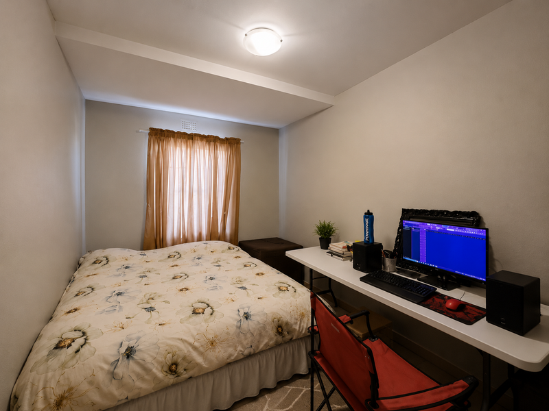 A compact bedroom featuring a neutral color palette, a window with curtains, and a ceiling light fixture, suitable for a guest room or office.