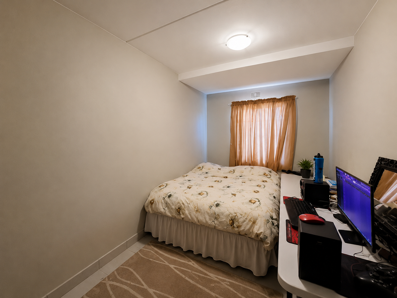 A compact bedroom featuring neutral walls, a window with curtains, and a ceiling vent, providing a functional space for rest or study.