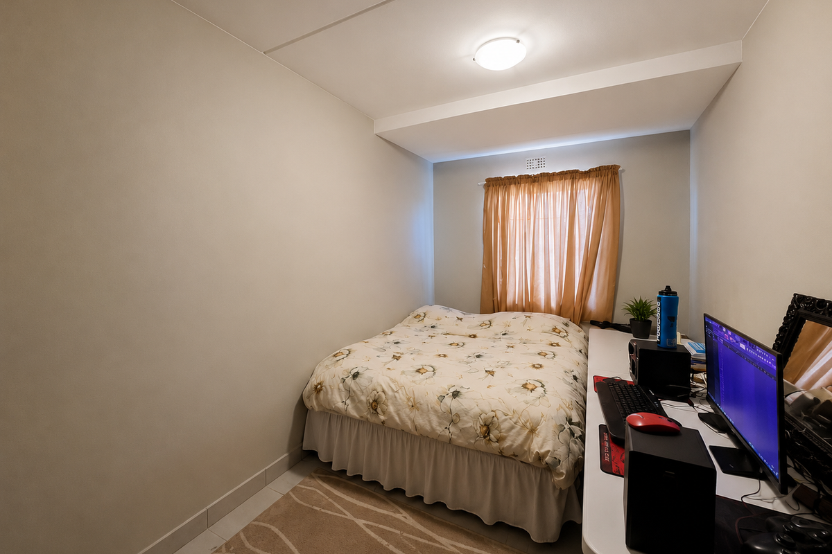 A compact bedroom featuring neutral walls, a window with curtains, and a ceiling vent, providing a functional space for rest or study.