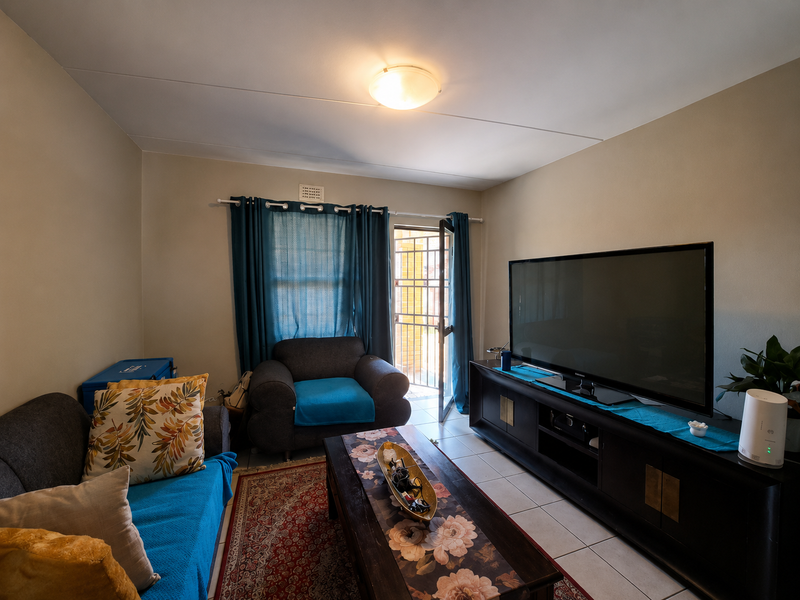 A comfortable living room featuring tiled flooring, a ceiling light fixture, and direct access to an outdoor area through a security gate.