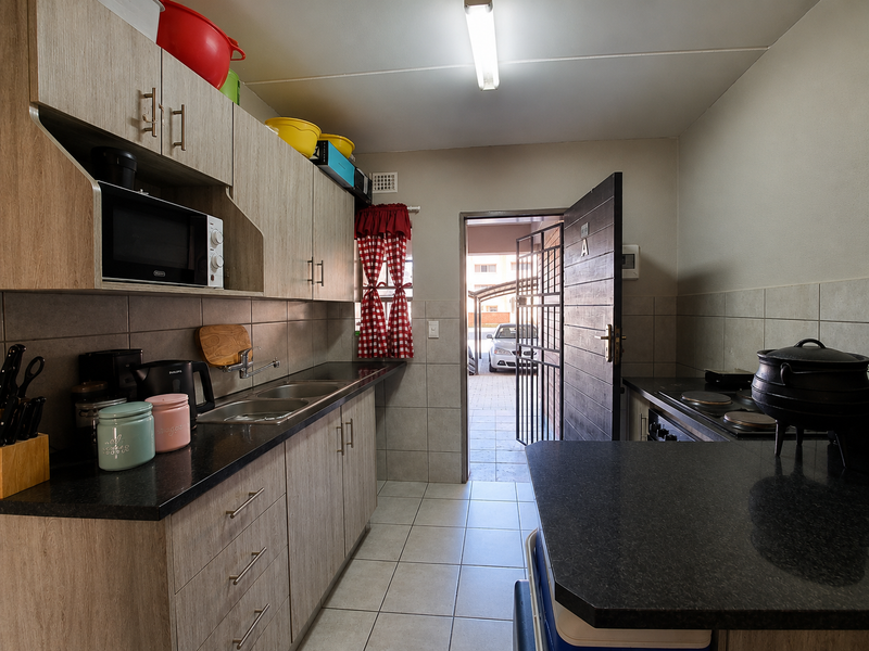 Functional kitchen featuring wood-look cabinetry, dark laminate countertops, tiled backsplash, and direct access to the exterior through a security gate.
