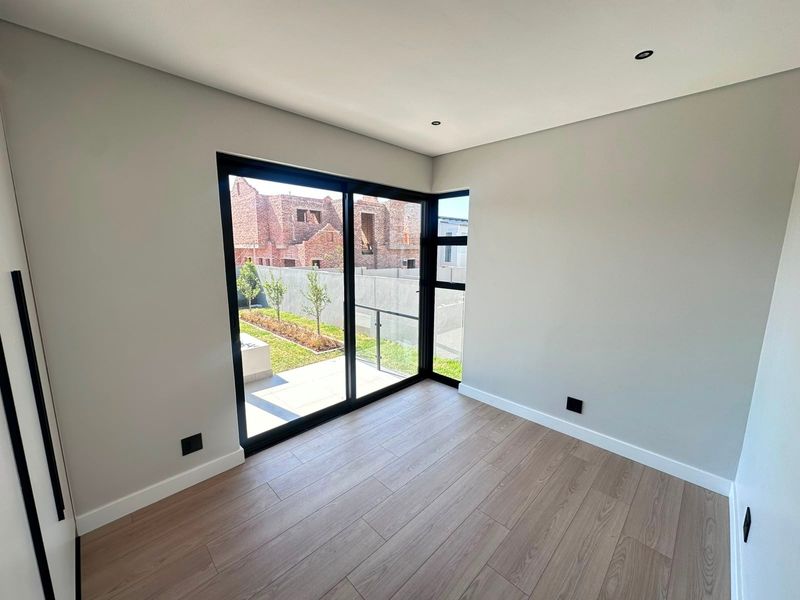 A bright, modern bedroom featuring laminate flooring, recessed lighting, and large black aluminium sliding doors that open to a private garden area.