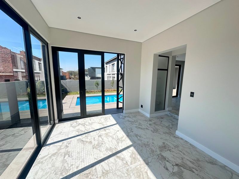 Bright, modern living area featuring large black aluminium sliding doors, marble-look floor tiles, and direct access to the outdoor swimming pool area.