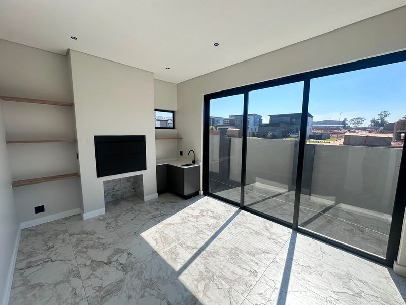 Modern living area featuring a built-in fireplace, floating shelving, a small wet bar with cabinetry, and large sliding doors opening to the exterior.
