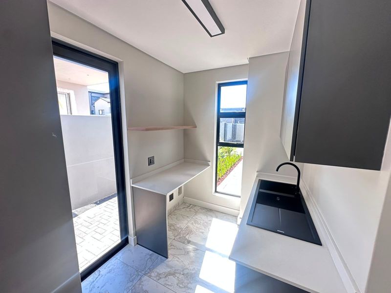 Modern scullery featuring sleek dark cabinetry, stone countertops, a black sink with matching tap, and direct access to the exterior via a sliding door.