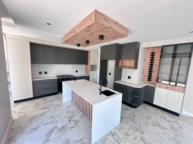 Modern, high-end kitchen featuring a central island, stone countertops, dark cabinetry, integrated gas stove, and stylish marble-look floor tiles.