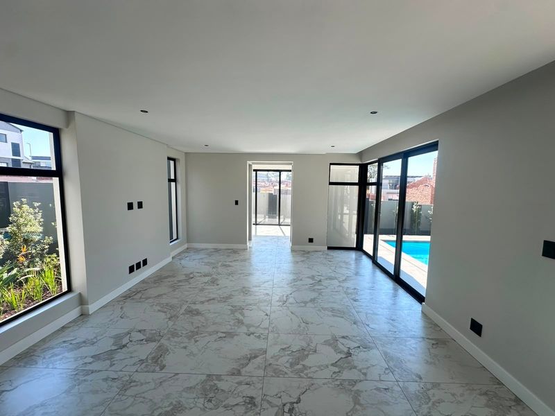 A bright, modern, and empty living area featuring large aluminium sliding doors, marble-look floor tiles, and direct access to the pool area.