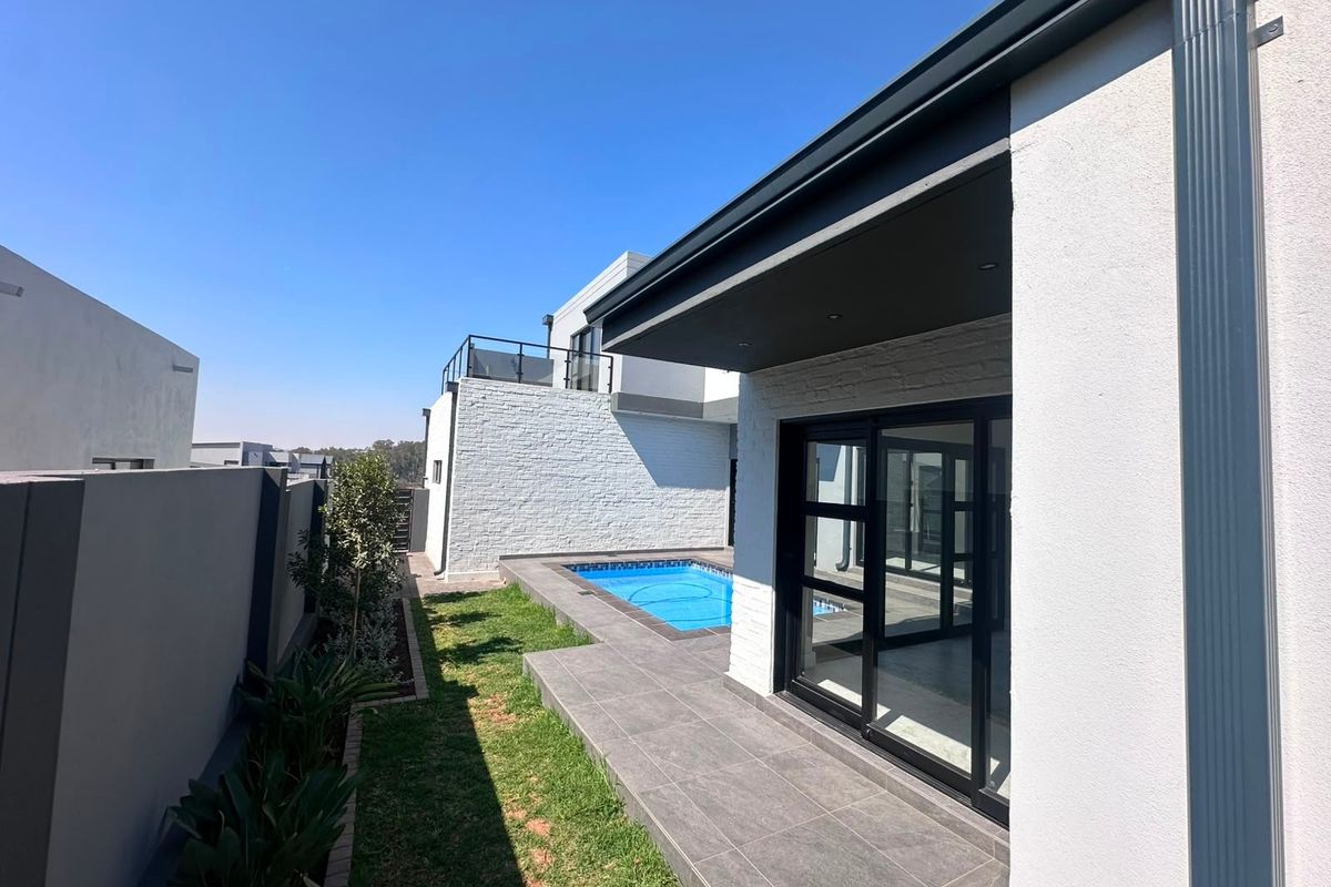 Rear exterior view featuring a modern tiled patio, swimming pool, and sliding glass doors leading into the home, set against a clean white facade.