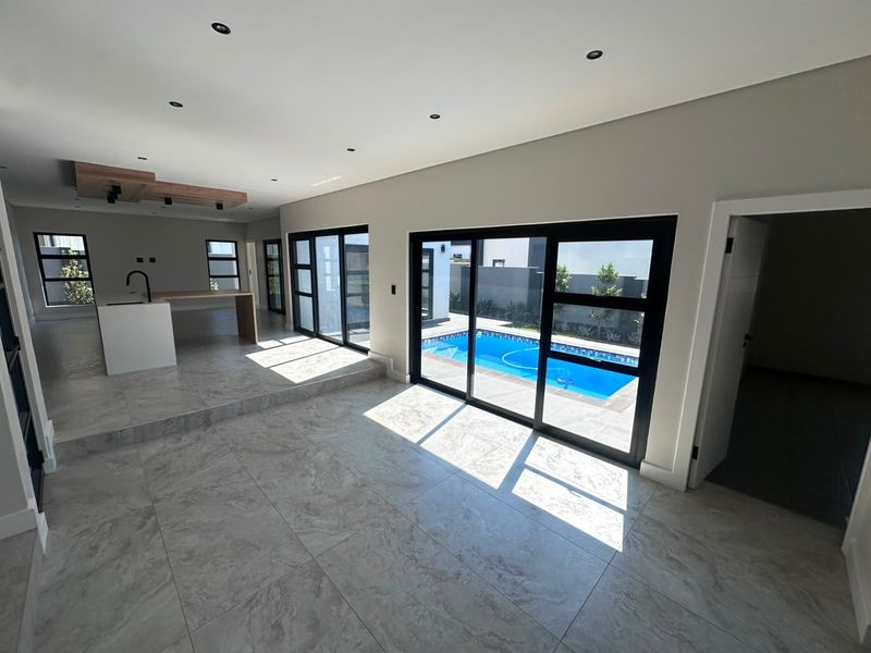 Spacious open-plan living and kitchen area featuring modern tiled flooring, recessed lighting, and large sliding glass doors opening directly to a private swimming pool.