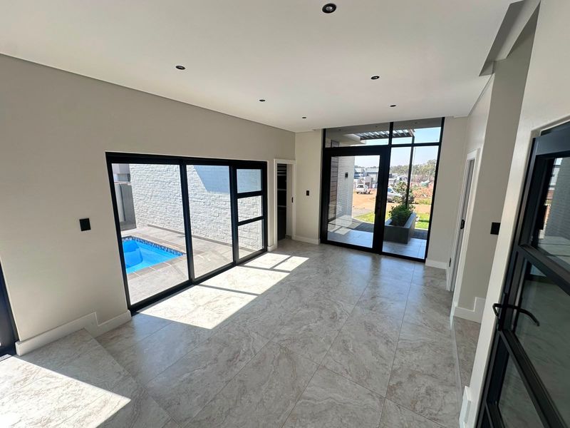 Modern, light-filled living area featuring large format floor tiles, recessed lighting, and expansive black aluminium sliding doors opening to a private pool area.