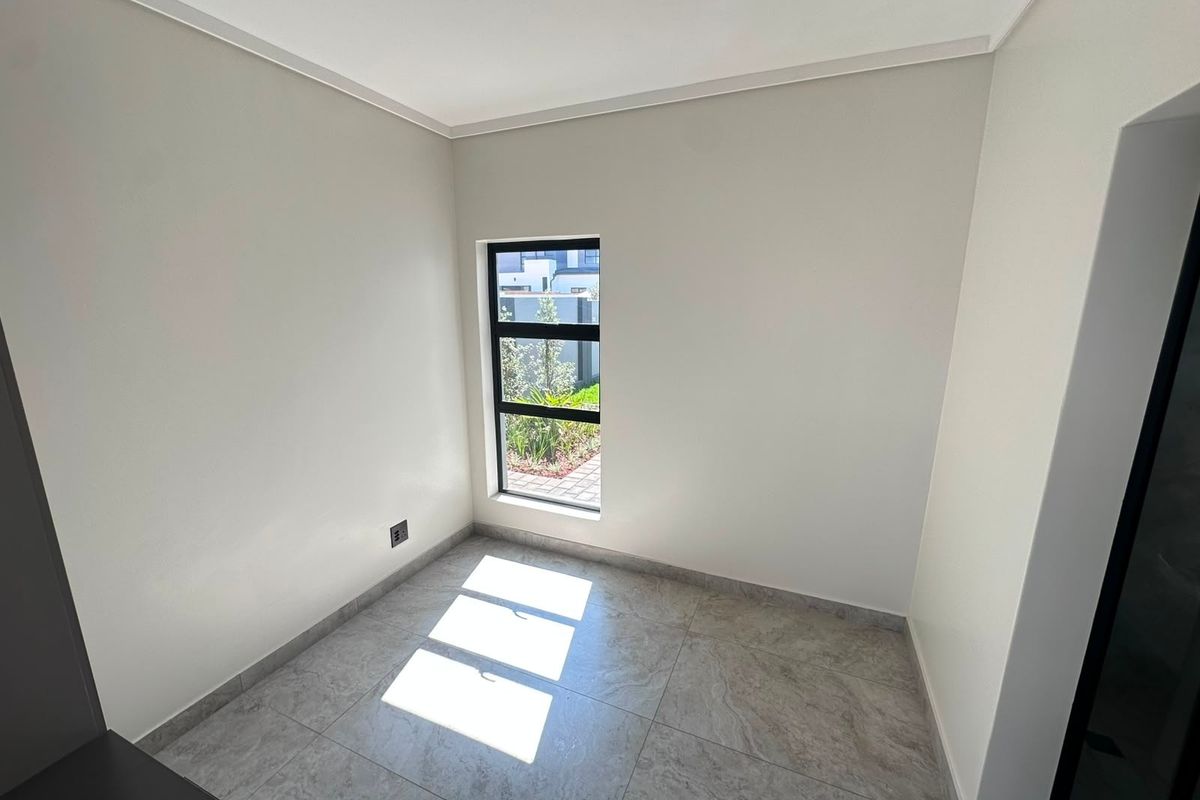 A bright, empty bedroom featuring modern neutral-toned floor tiles and a sleek aluminium-framed window.