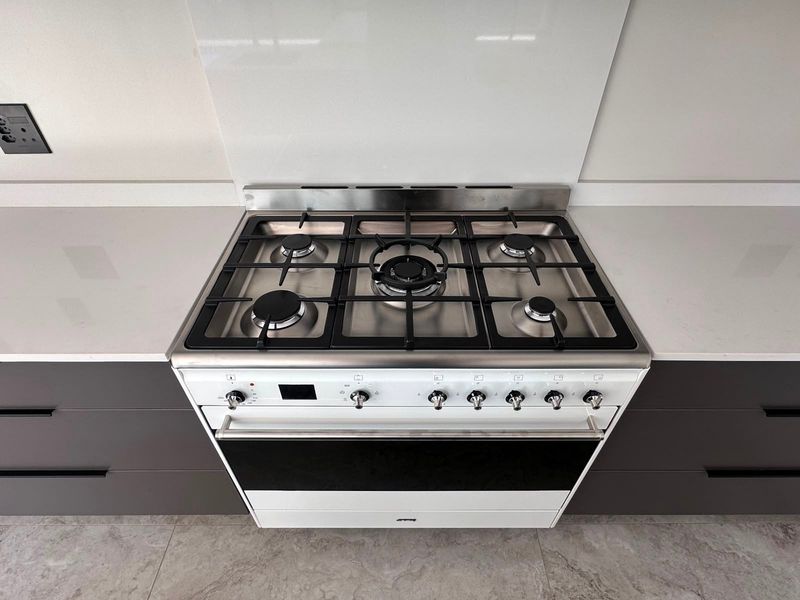 Modern kitchen featuring a high-end gas cooktop, integrated oven, sleek stone benchtops, and contemporary dark cabinetry with a clean glass splashback.