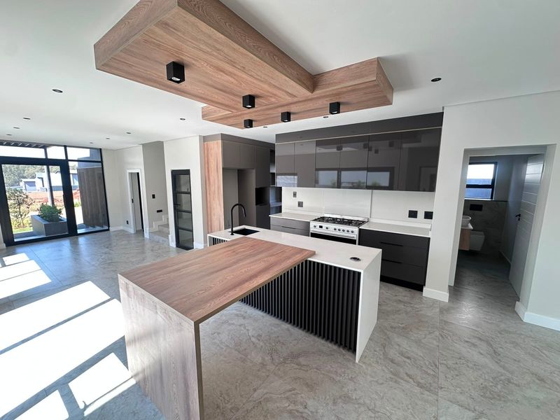 Modern open-plan kitchen featuring a large island with wood-look breakfast bar, sleek dark cabinetry, gas stove, and stylish recessed ceiling lighting.