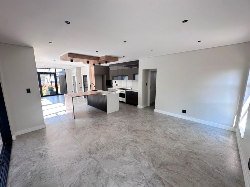 Modern open-plan kitchen and living area featuring a central island, sleek cabinetry, gas stove, and contemporary tiled flooring with recessed lighting.