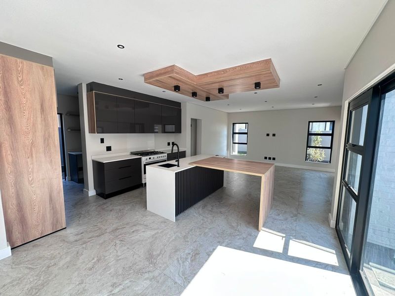 Modern open-plan kitchen and living area featuring a central island, sleek cabinetry, gas stove, and a unique timber-accented recessed ceiling design.