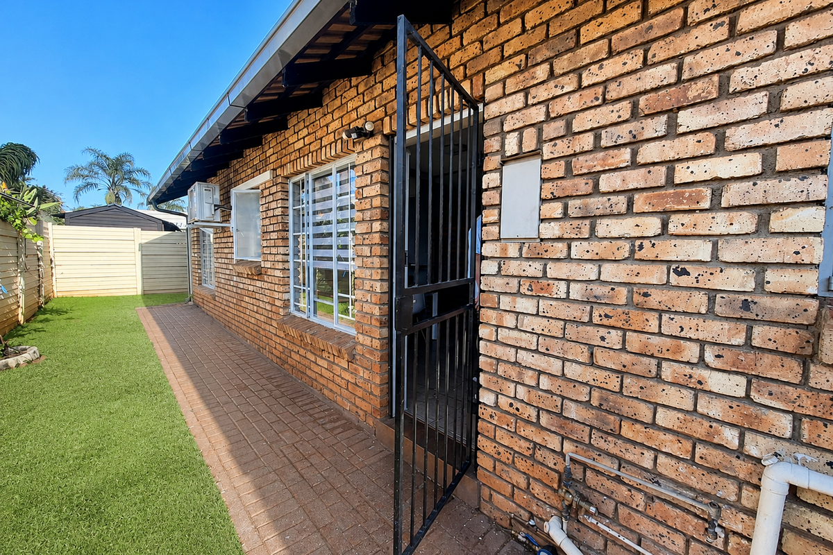 Rear exterior view of the townhouse featuring exposed brick walls, a paved walkway, security gate, and external plumbing fixtures.