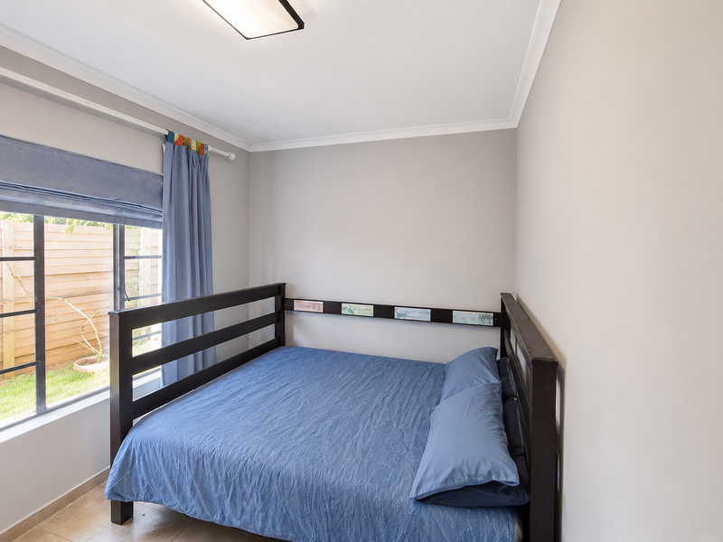 A well-maintained bedroom featuring neutral wall tones, tiled flooring, and a large window providing natural light and a view of the garden area.