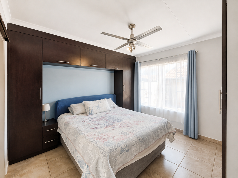 A well-maintained bedroom featuring extensive dark wood built-in cabinetry, tiled flooring, and a ceiling fan, offering a functional and organized living space.