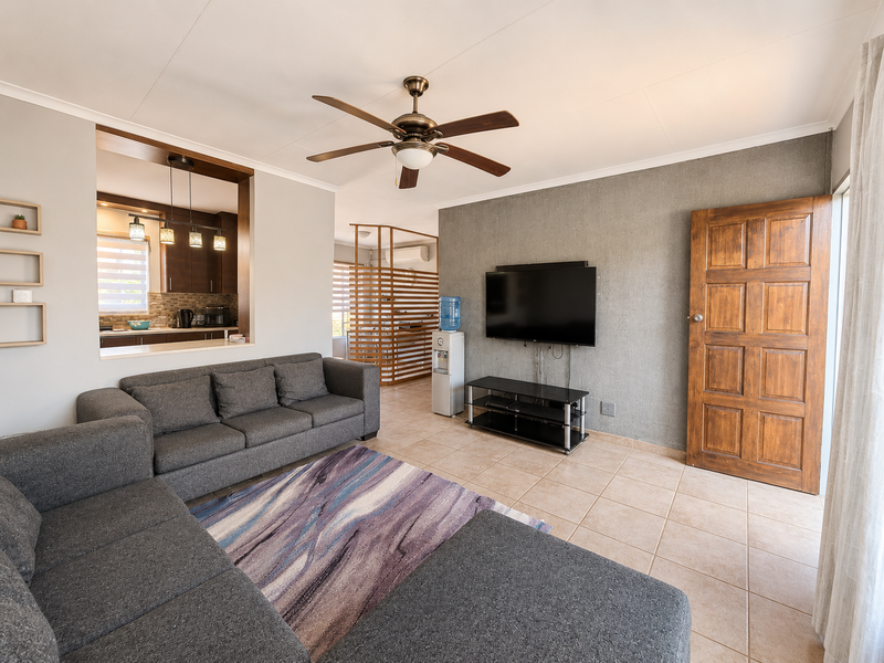 Open-plan living area featuring tiled flooring, a ceiling fan, and a textured feature wall, with a convenient pass-through window connecting to the kitchen.