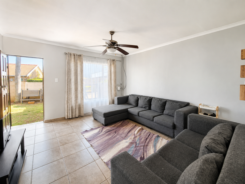 A bright living room featuring tiled flooring, a ceiling fan, and direct access to the outdoor garden area through a sliding door.
