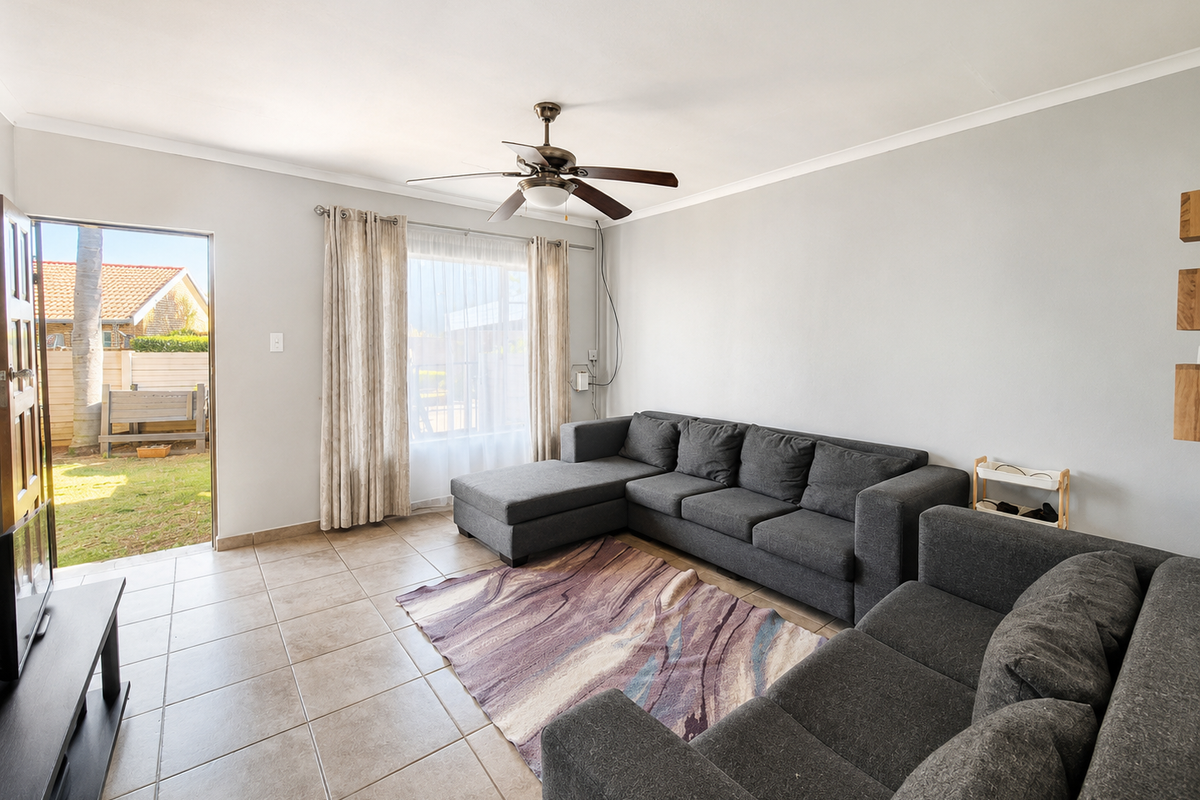 A bright living room featuring tiled flooring, a ceiling fan, and direct access to the outdoor garden area through a sliding door.