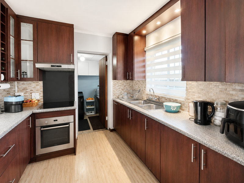 A well-maintained kitchen featuring dark wood cabinetry, granite countertops, stainless steel appliances, and a tiled backsplash, with an adjacent laundry area.