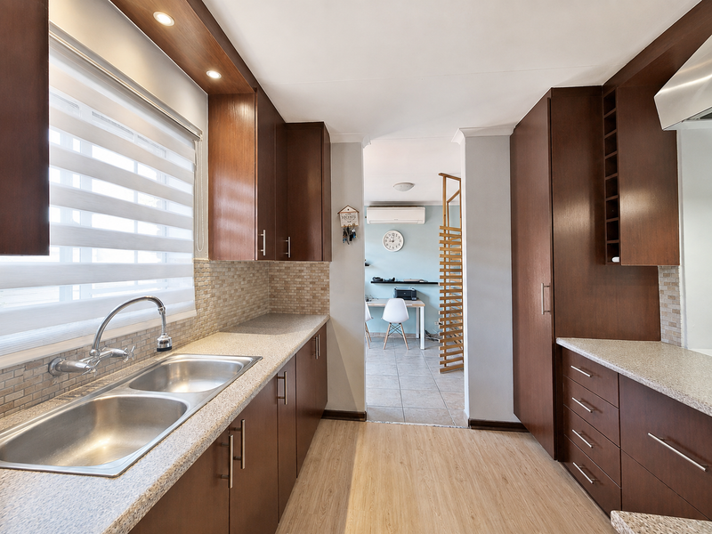 A well-maintained kitchen featuring dark wood cabinetry, stone-look countertops, a double basin sink, and a mosaic tile backsplash with modern recessed lighting.