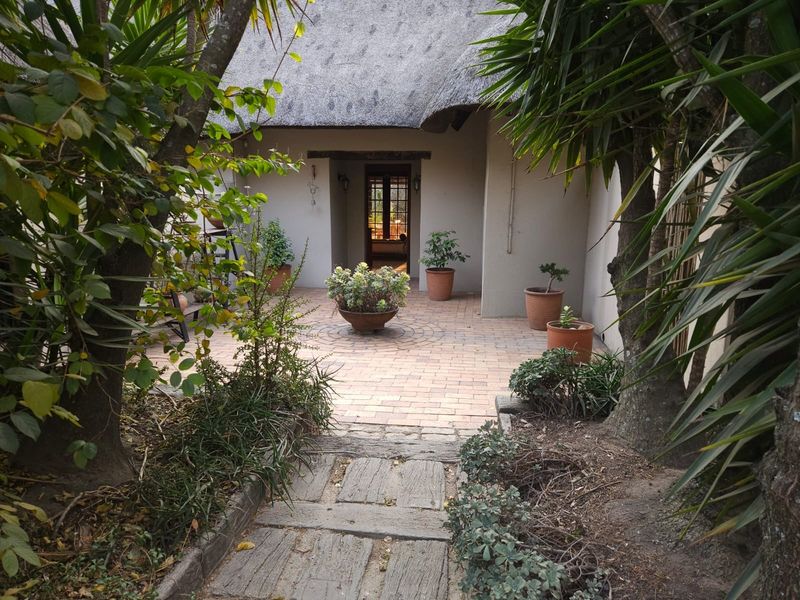 A charming rear patio area featuring a traditional thatched roof, brick paving, and a stone pathway leading to the entrance.