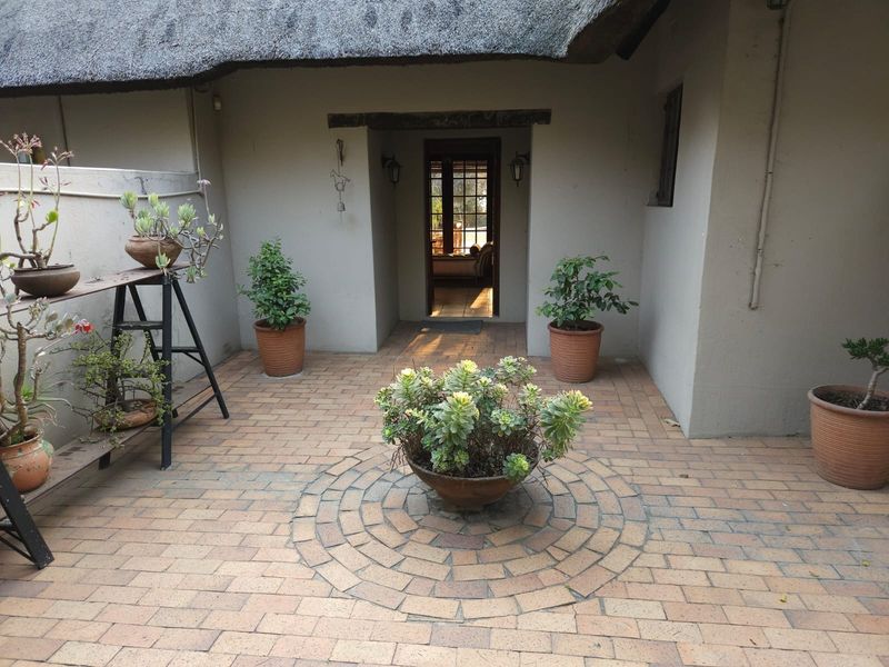 A covered patio area featuring a traditional thatched roof and decorative circular brick paving, providing a welcoming entrance to the home.