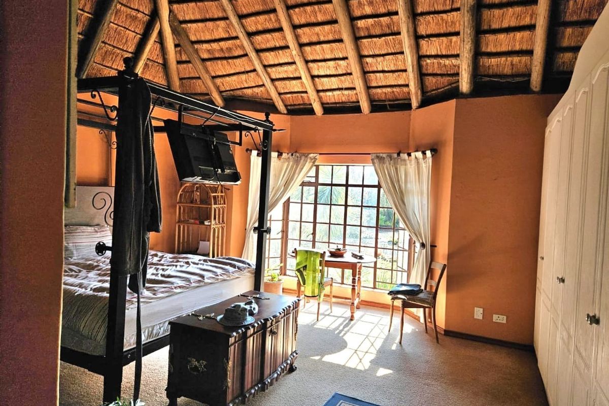 Spacious bedroom featuring a high thatched roof with exposed timber rafters, built-in cupboards, and large grid-pattern windows allowing for natural light.