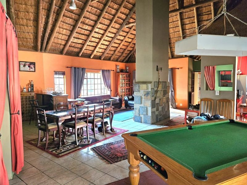 Spacious open-plan living and dining area featuring a high thatched roof with exposed rafters and a prominent stone-clad central fireplace.