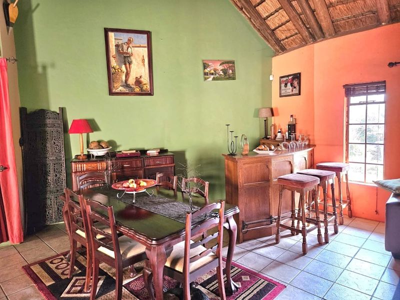Open plan living and dining area featuring a built-in bar, tiled flooring, and a high vaulted ceiling with exposed timber rafters and thatch.