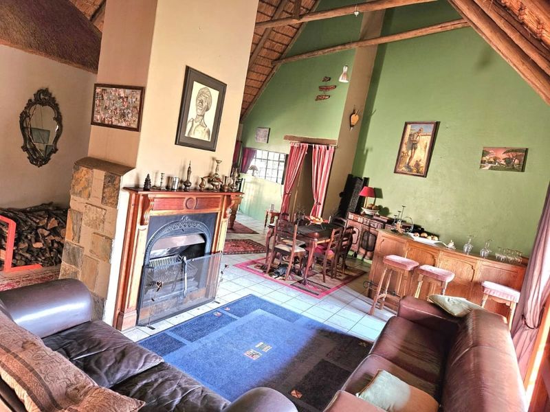 Spacious open-plan living and dining area featuring a high thatched roof with exposed timber trusses, a central fireplace, and stone-clad accents.