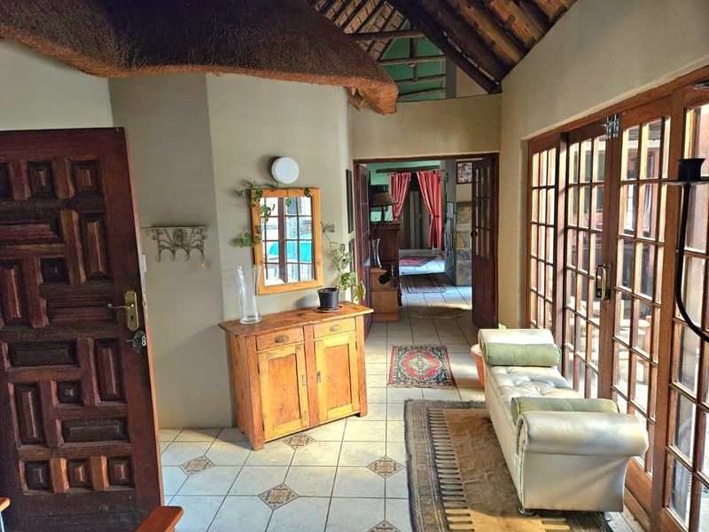 Entrance hall featuring a traditional thatched roof with exposed rafters, ceramic tiled flooring, and large wooden-framed glass doors leading to the exterior.