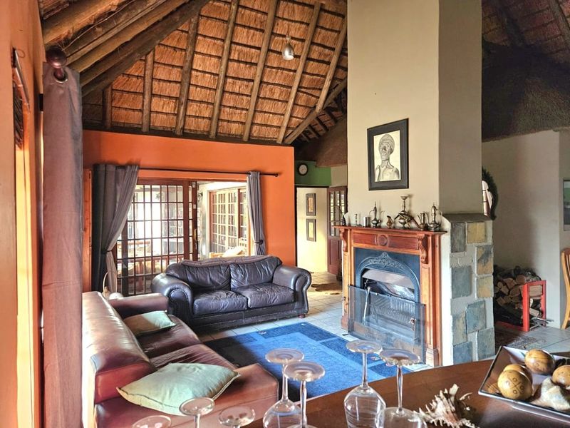 Spacious living room featuring a high vaulted thatched ceiling with exposed rafters, a prominent stone-clad fireplace, and large french doors leading to the patio.