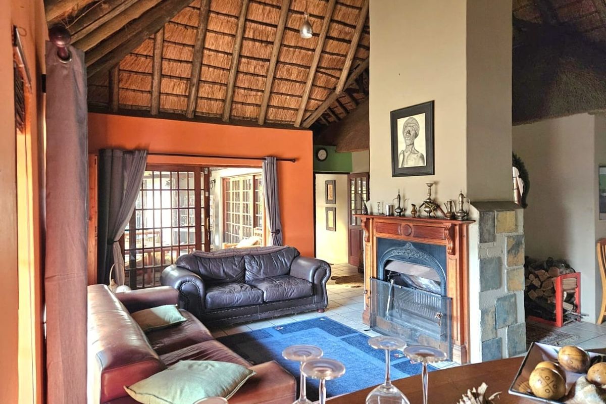 Spacious living room featuring a high vaulted thatched ceiling with exposed rafters, a prominent stone-clad fireplace, and large french doors leading to the patio.
